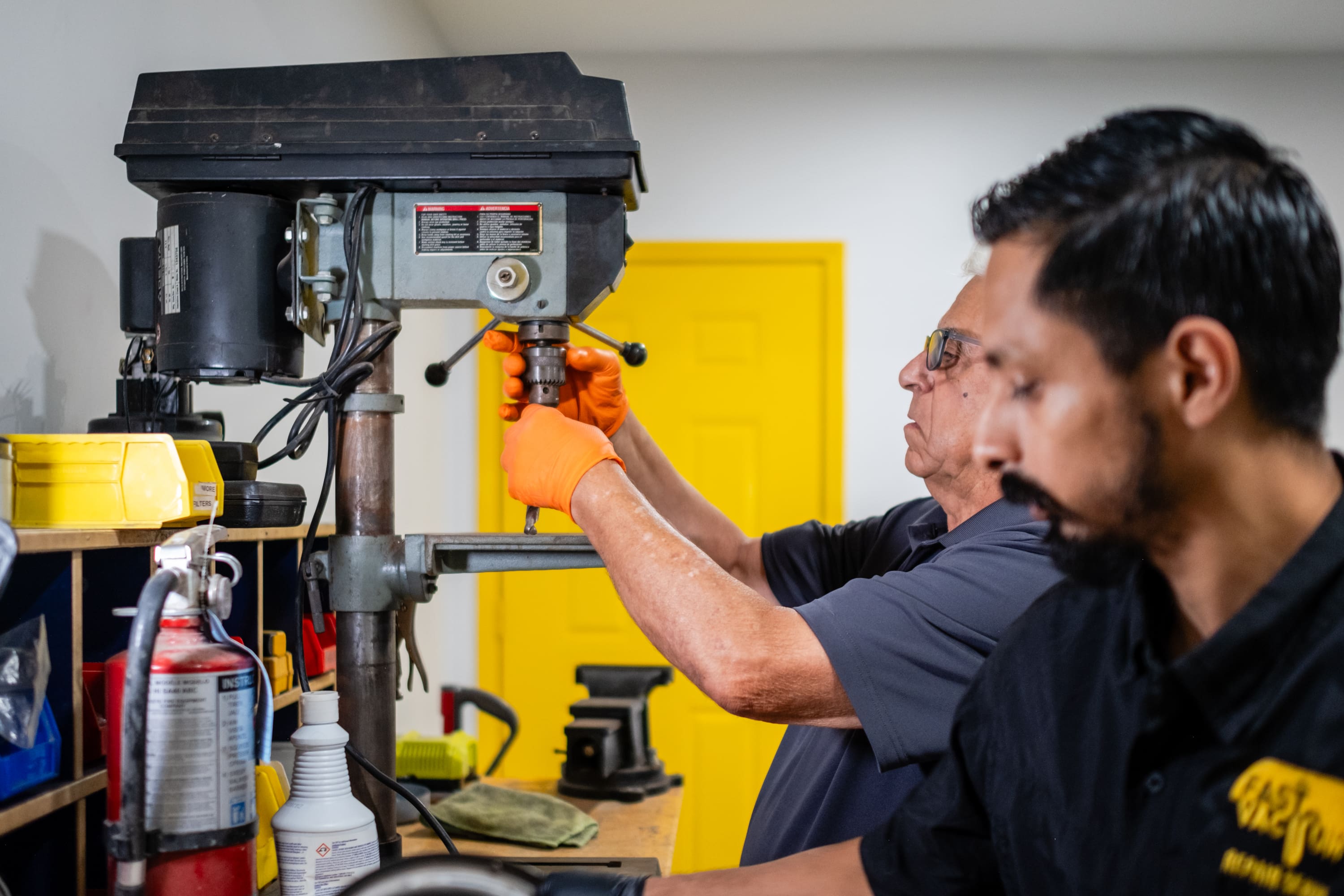 Two men working on a drill press.